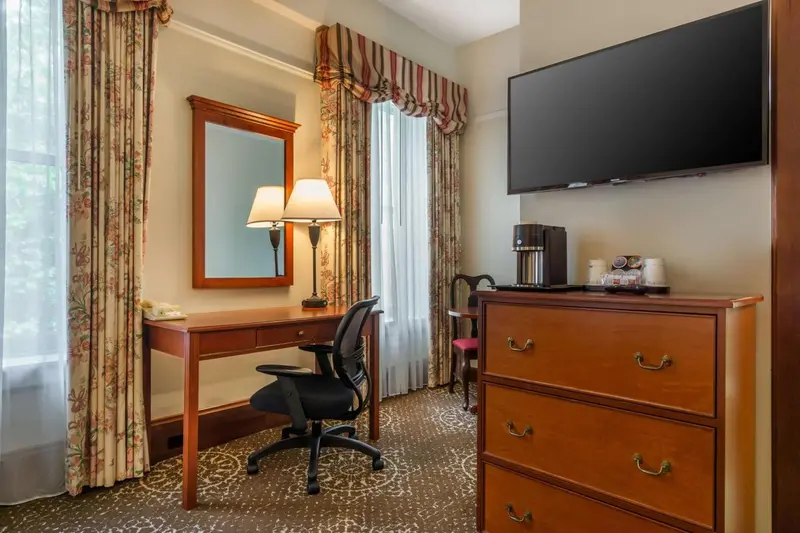 Une chambre d'hôtel avec un bureau, une commode et une télévision murale.