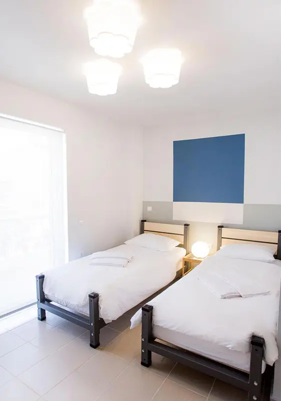 Une chambre lumineuse avec deux lits simples et un mur bleu.