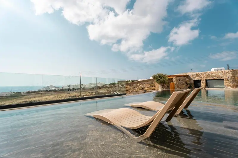 Deux transats en bois se trouvent au bord d'une piscine à débordement avec vue sur la mer.