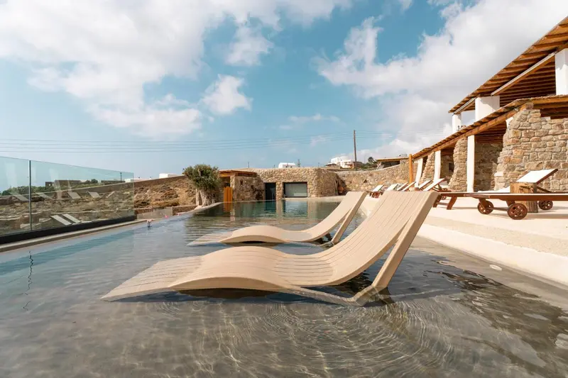 Transats en bois clair bordent une piscine à débordement avec vue sur la mer.