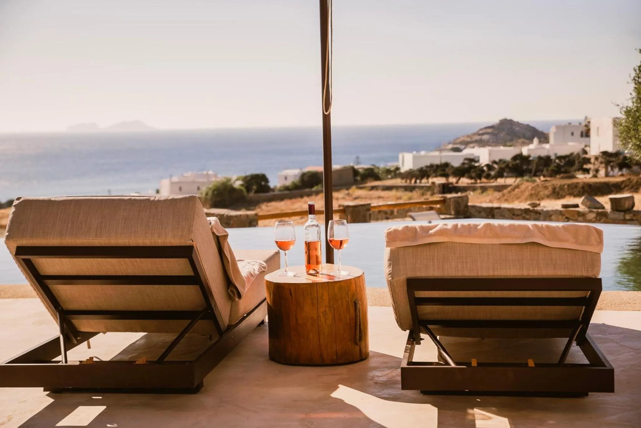 Deux transats avec des verres sur une table basse au bord d'une piscine à débordement avec vue sur la mer.