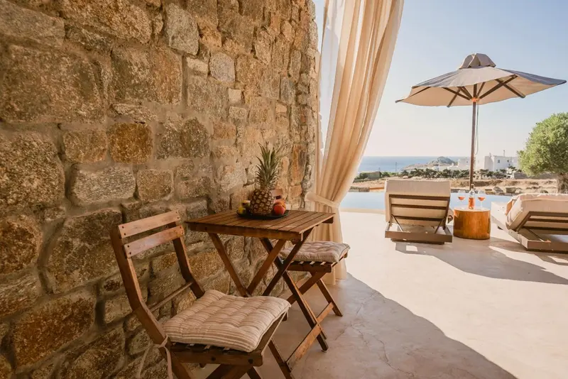 Une table et des chaises en bois sont disposées sur une terrasse avec une vue sur la mer.