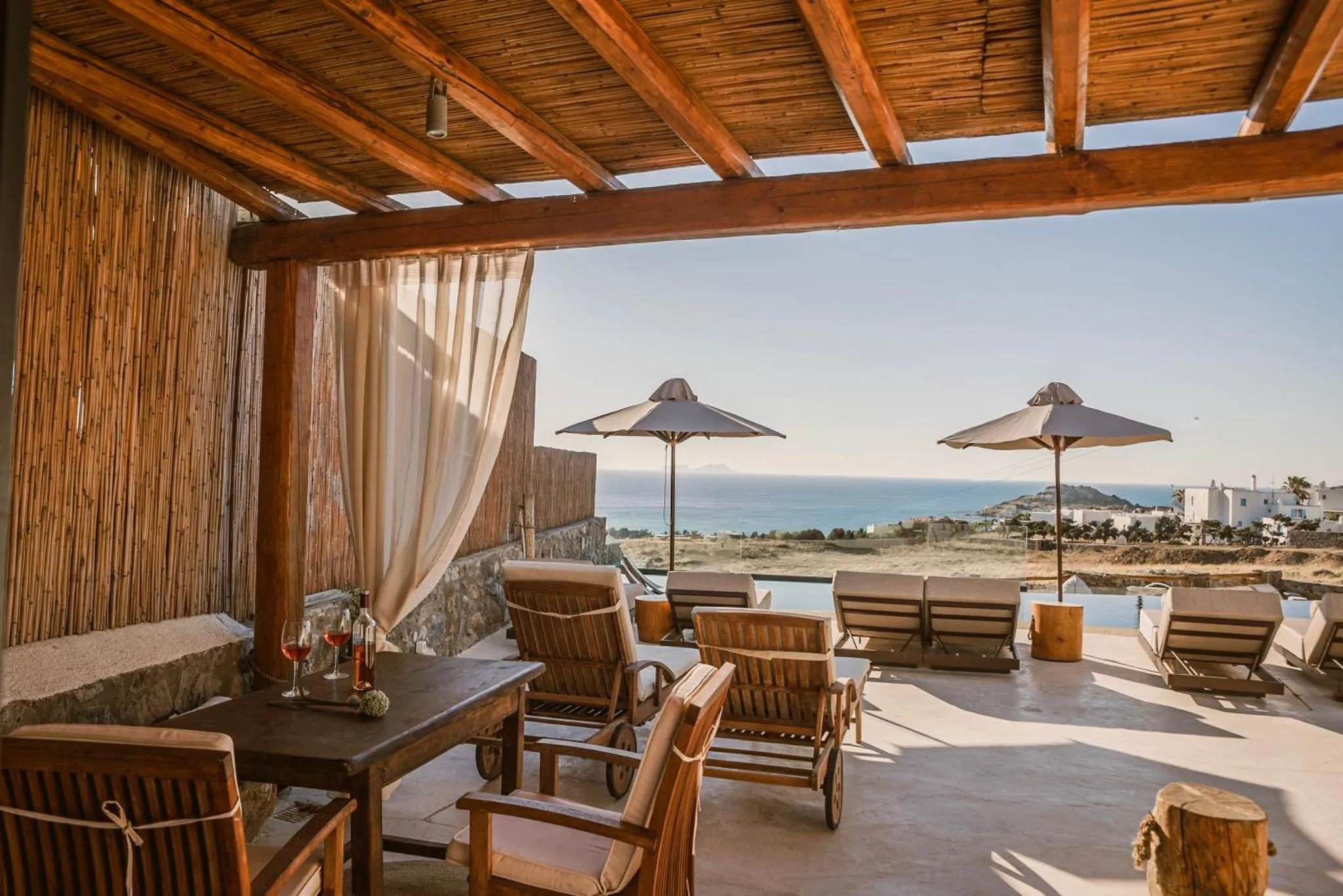 Terrasse ombragée avec mobilier de détente et vue sur la mer.