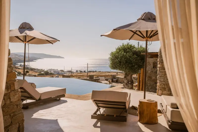 Transats et piscine à débordement avec vue sur la mer et les collines.