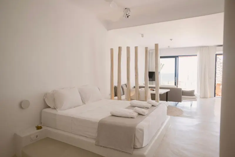 Une chambre lumineuse avec un grand lit et un espace salon ouvert sur une vue mer.