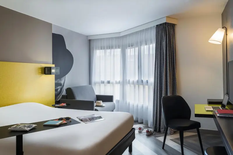Une chambre lumineuse avec un lit, un bureau et un fauteuil.