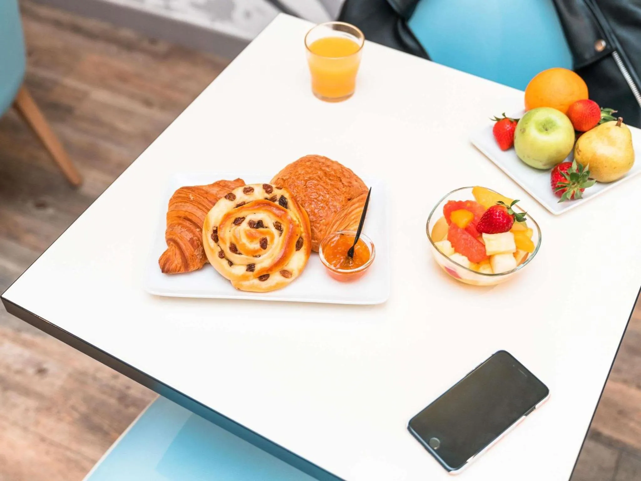 Une table blanche présente un petit-déjeuner avec des viennoiseries, des fruits et une boisson.
