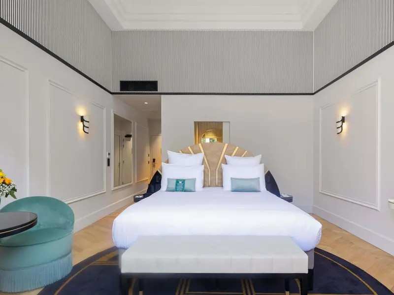 Une chambre lumineuse avec un grand lit et un fauteuil turquoise.