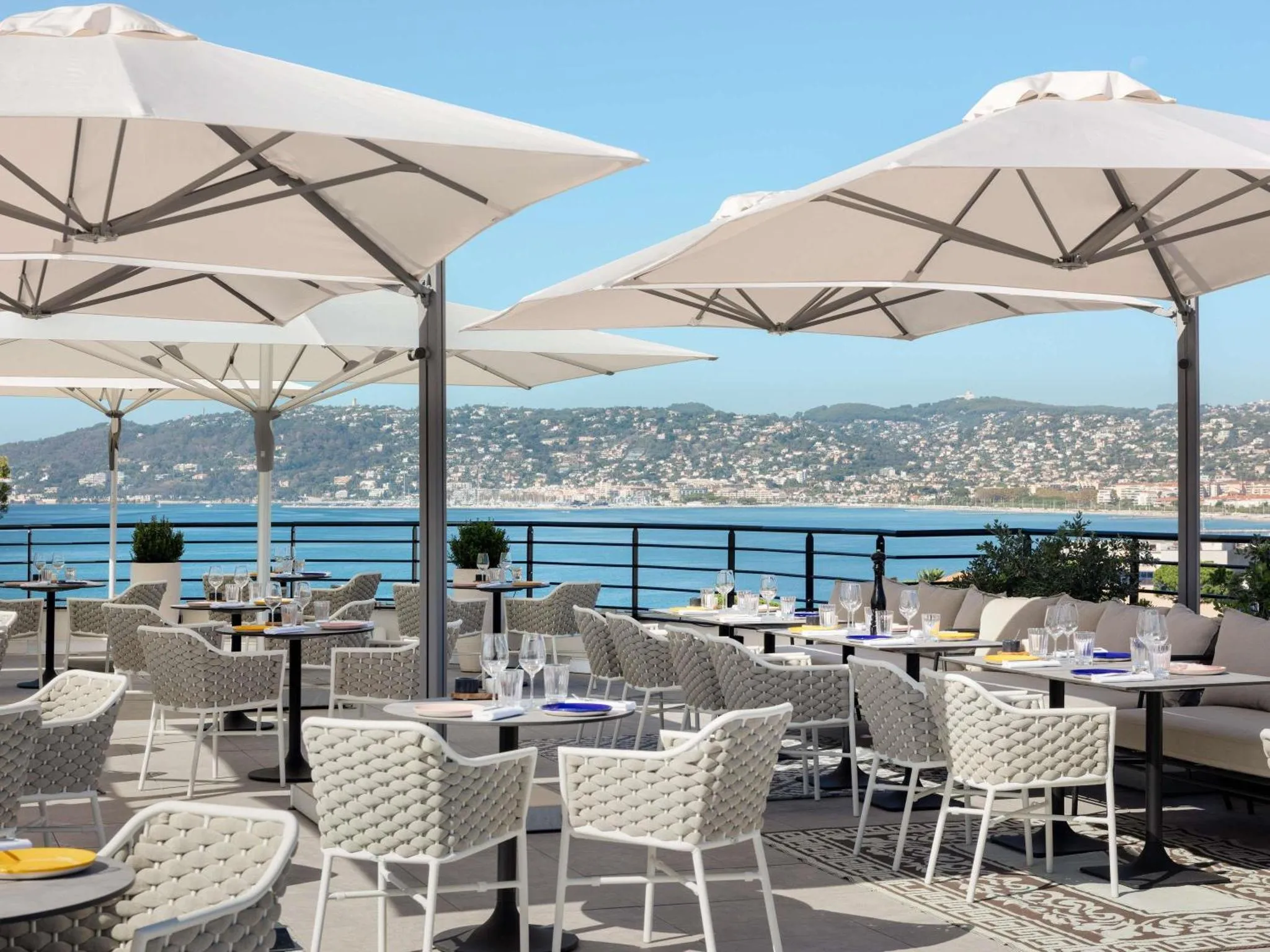 Terrasse ombragée avec tables et chaises donnant sur la mer et les collines.