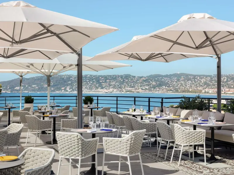 Terrasse ombragée avec tables et chaises donnant sur la mer et les collines.