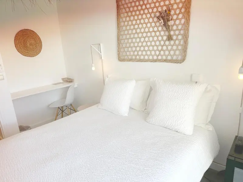 Une chambre lumineuse avec un lit blanc et des éléments décoratifs en fibres naturelles.