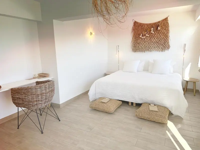 Une chambre lumineuse avec un grand lit blanc et un bureau en osier.