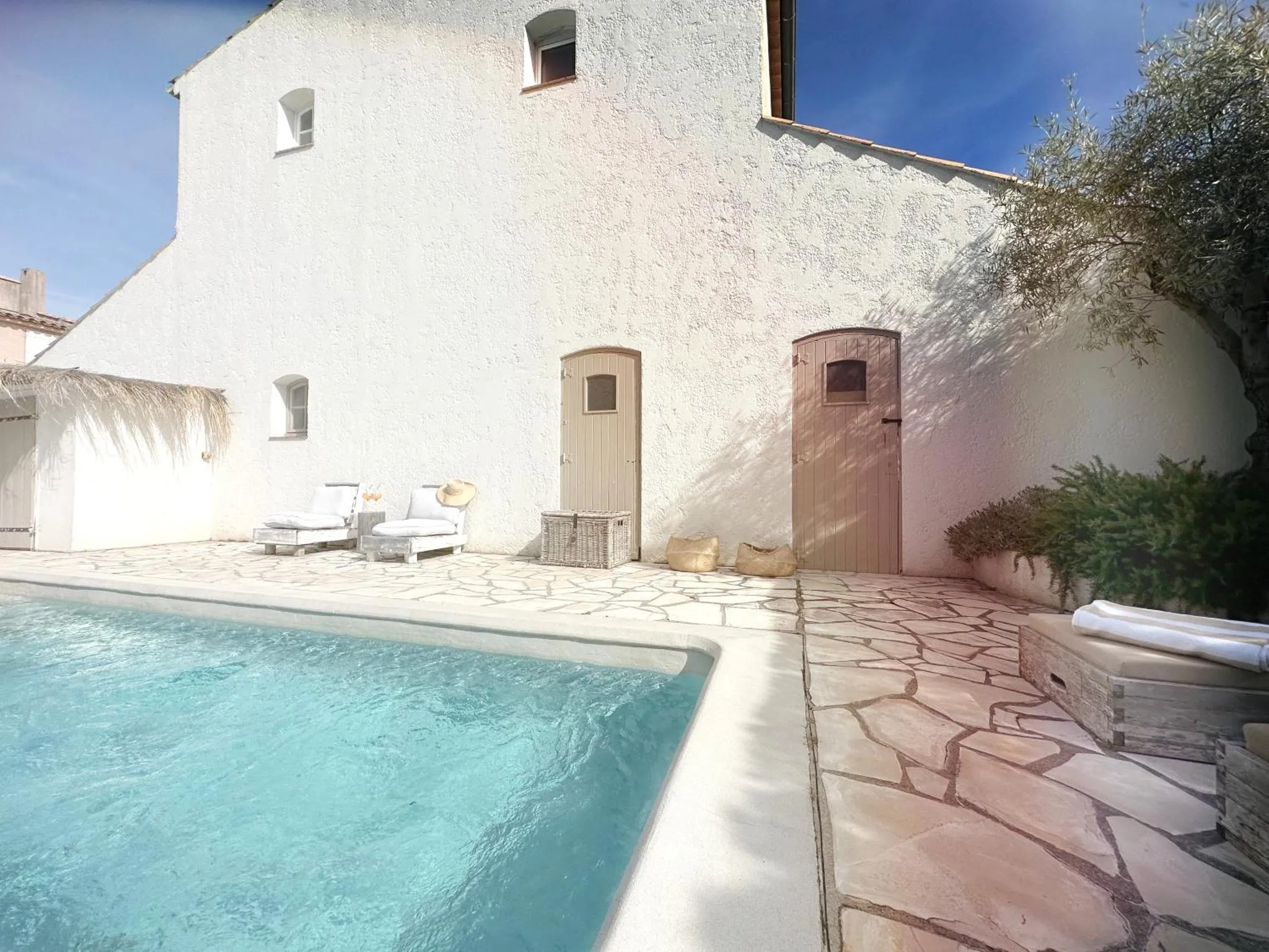 Une piscine turquoise bordée d'une terrasse pavée et de quelques transats.