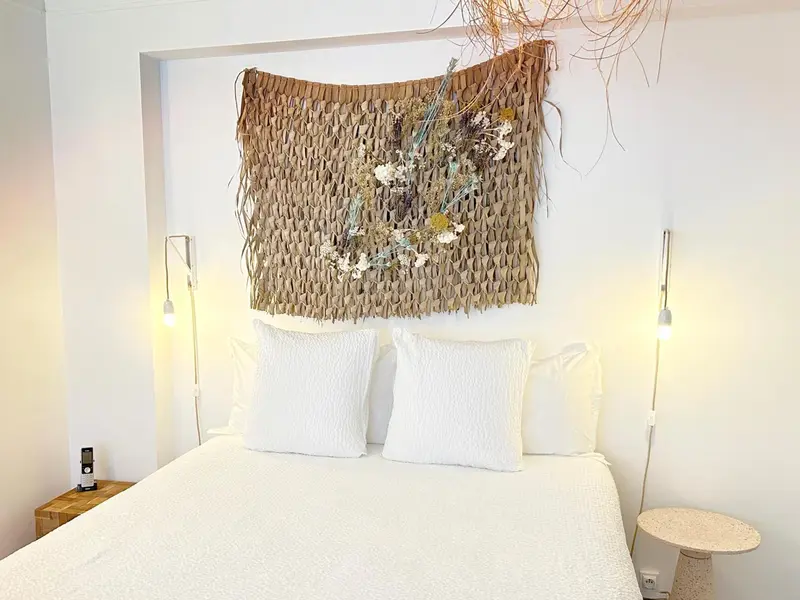 Un lit blanc est orné d'une décoration murale en fibres naturelles et de deux lampes de chevet.