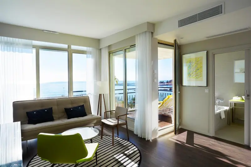 Espace de séjour lumineux avec canapé et accès à un balcon ensoleillé.
