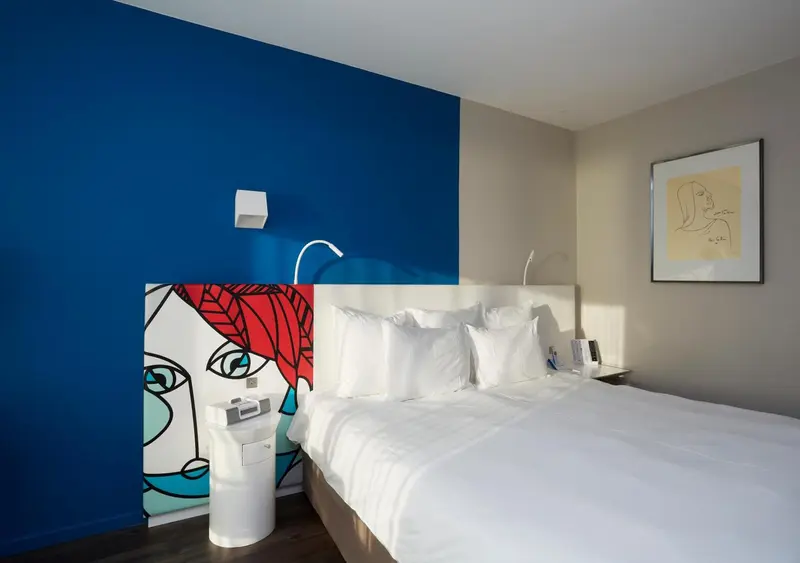 Une chambre lumineuse avec un lit blanc et une décoration murale colorée.