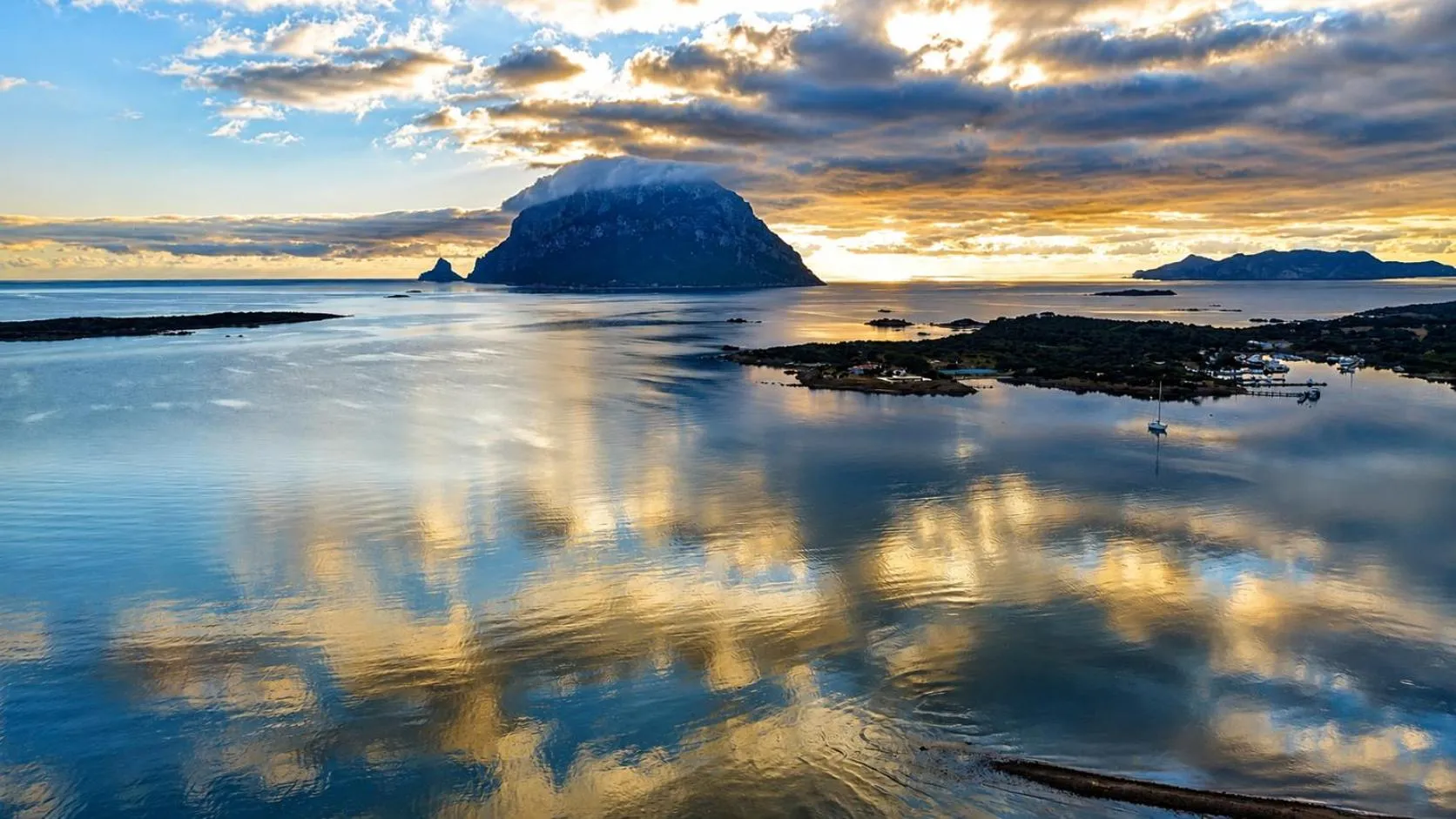 Paysage marin au coucher du soleil avec une île rocheuse et des reflets dans l'eau.