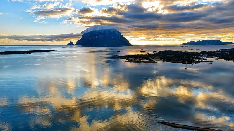 Paysage marin au coucher du soleil avec une île rocheuse et des reflets dans l'eau.