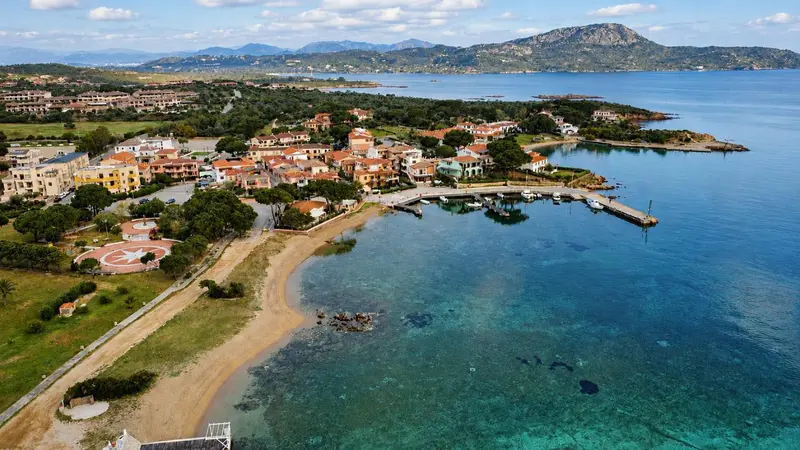 Vue aérienne d'un village côtier avec des bâtiments aux toits rouges et une plage de sable.