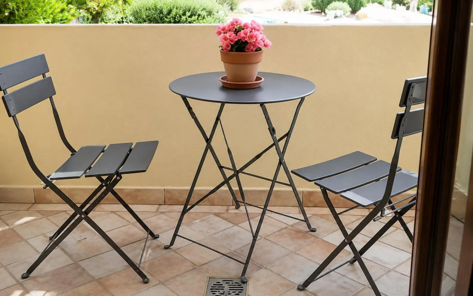 Une table ronde et deux chaises en métal sur une terrasse carrelée.
