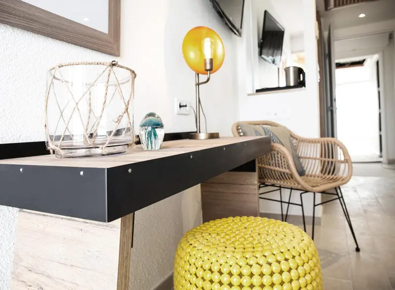 Une table de chevet avec une lampe et un pouf jaune dans une chambre.