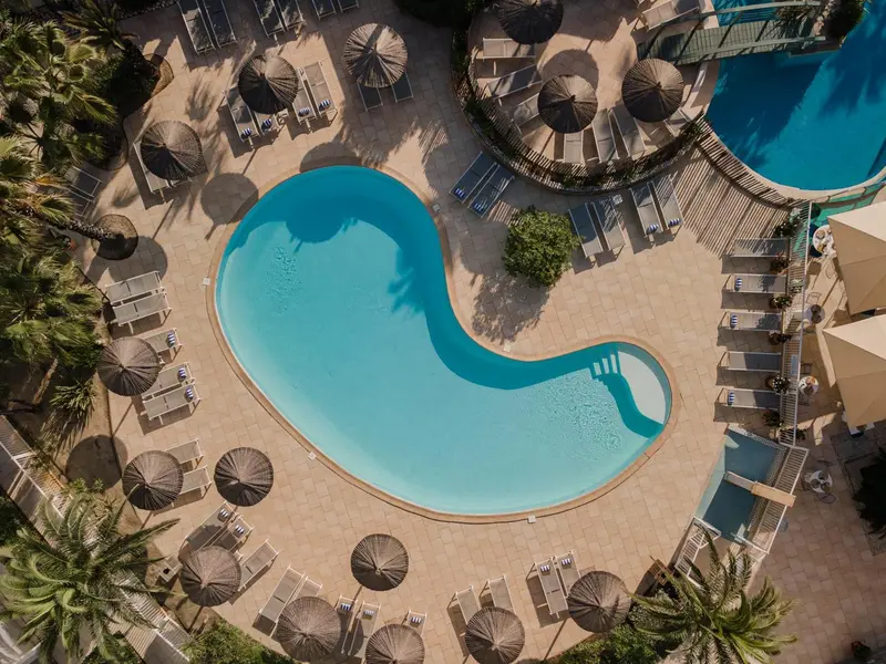 Vue aérienne d'une piscine sinueuse entourée de transats et de parasols.