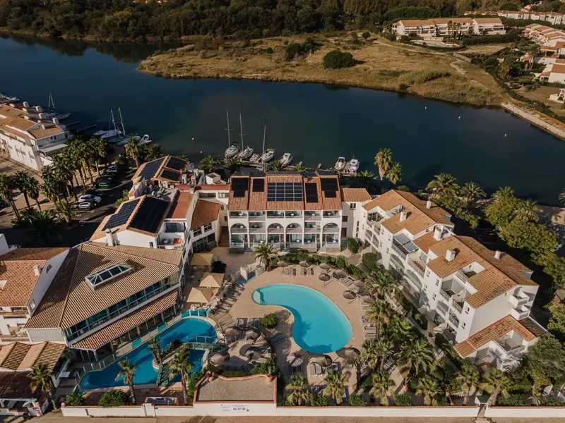 Vue aérienne d'un complexe hôtelier blanc et ocre avec piscine et végétation luxuriante.
