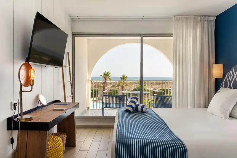 Une chambre lumineuse avec un lit et un bureau donnant sur une vue mer.
