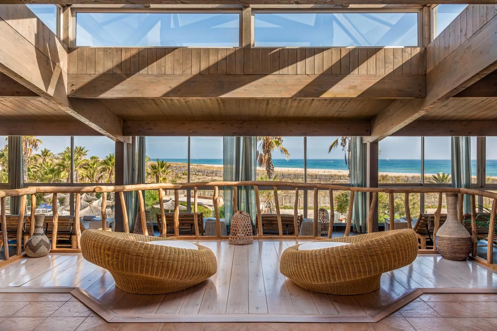 Espace de détente intérieur avec mobilier en rotin et vue sur la mer.