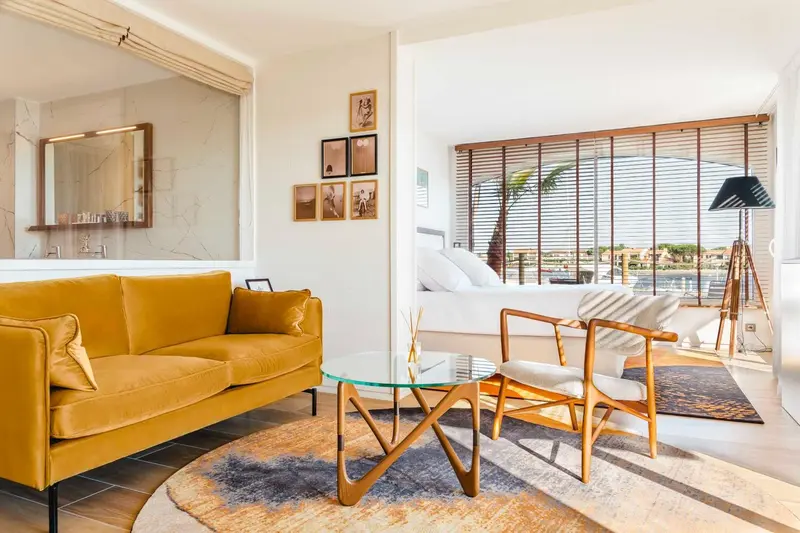 Un salon lumineux avec un canapé jaune et des fauteuils en bois.