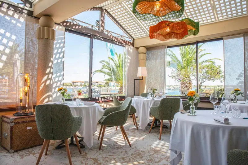 Une salle à manger lumineuse avec des tables nappées et une vue sur la mer.