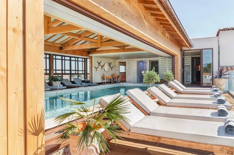 Transats et palmiers bordent une piscine intérieure lumineuse.