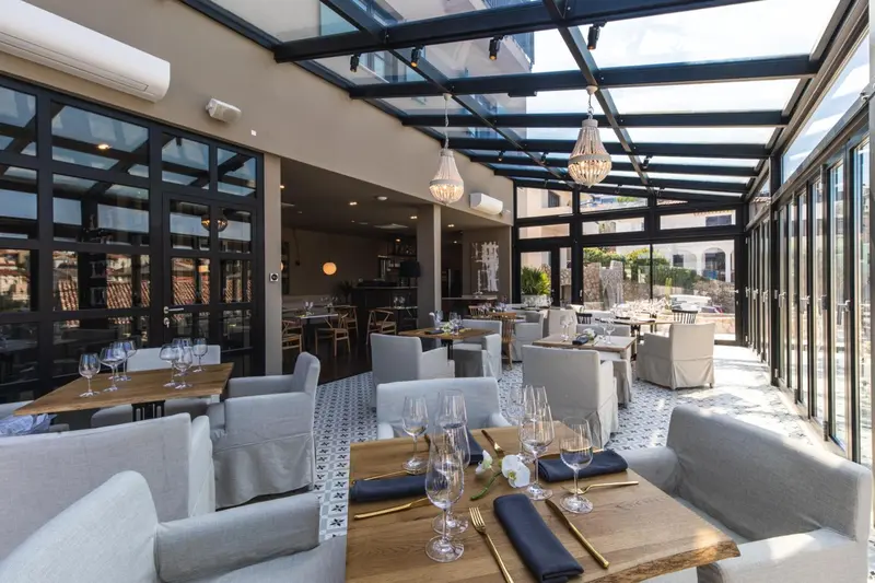 Une salle à manger lumineuse avec de grandes baies vitrées et des tables dressées.