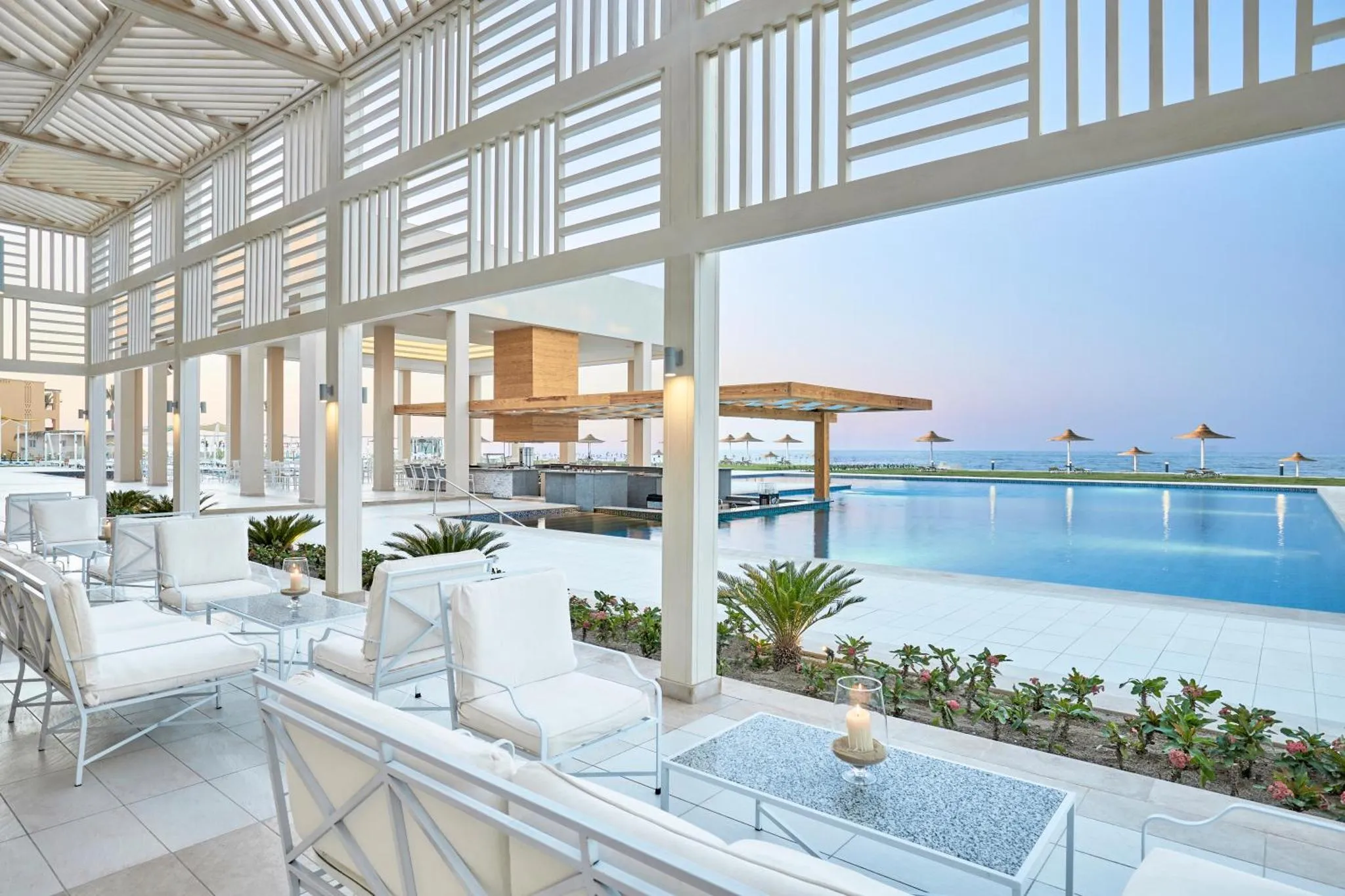 Espace de détente extérieur avec mobilier blanc et piscine à débordement.