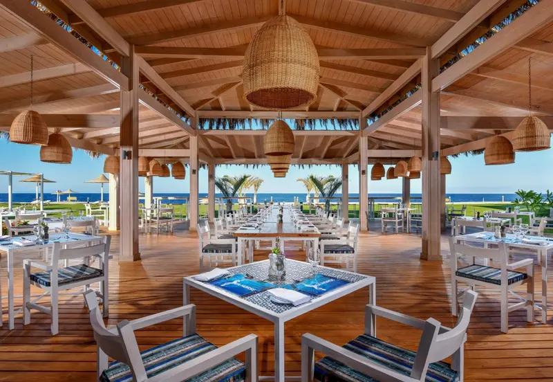 Une salle à manger extérieure avec des tables dressées face à la mer.