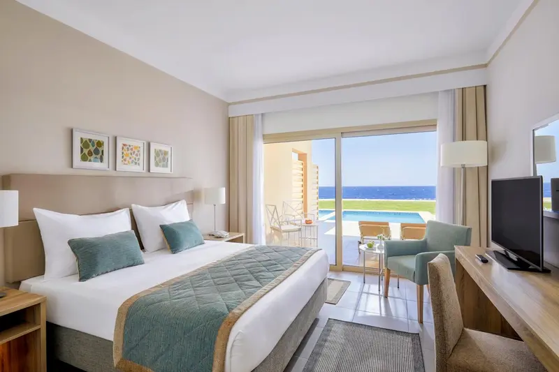 Une chambre lumineuse avec un grand lit donnant sur une terrasse et une piscine.