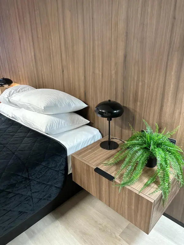 Un lit avec oreillers blancs et une table de chevet en bois avec une plante verte.