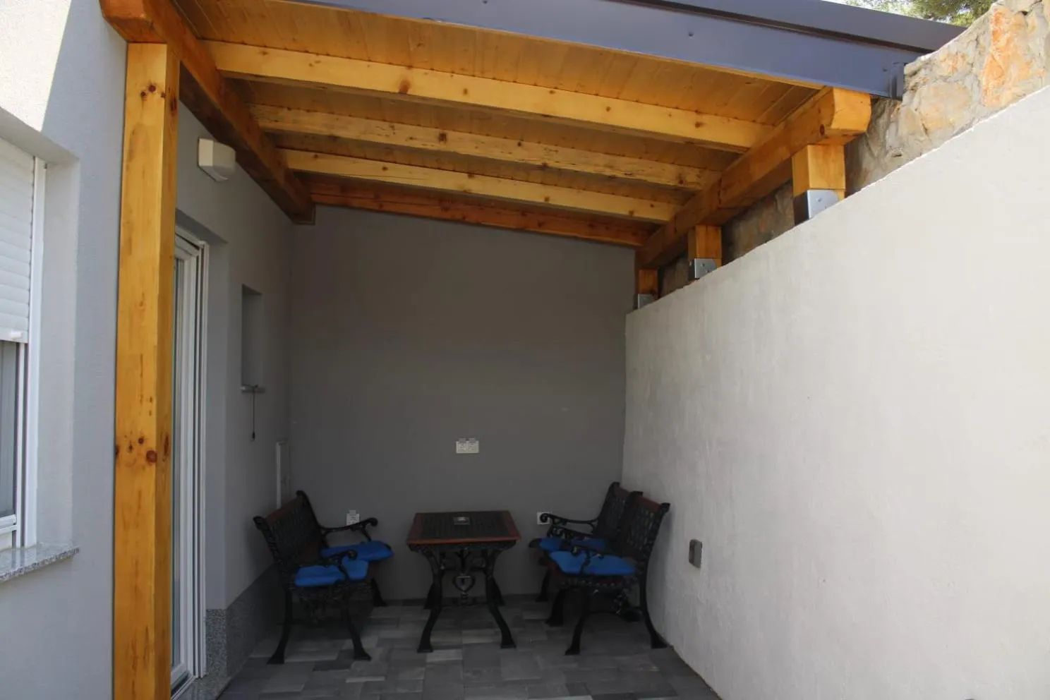 Petite terrasse ombragée avec table et chaises en fer forgé.