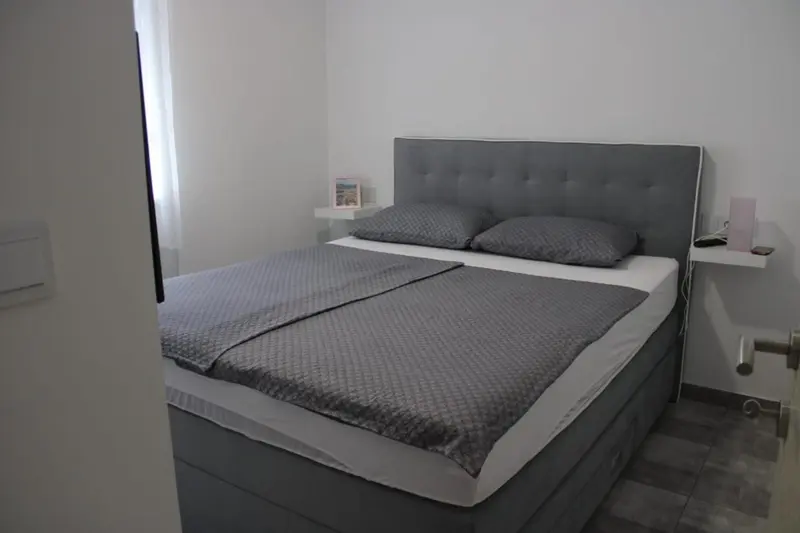 Une chambre avec un grand lit recouvert d'une couverture grise et de deux oreillers.