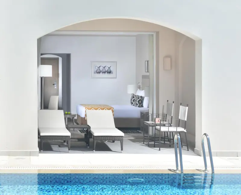 Une chambre lumineuse s'ouvre sur une terrasse avec chaises longues et piscine.