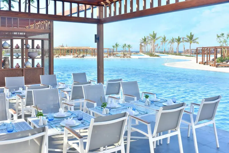 Tables dressées en terrasse au bord d'une piscine turquoise.