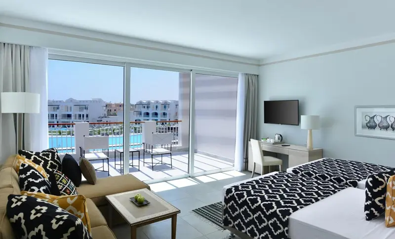 Une chambre lumineuse avec un canapé et un accès à une terrasse avec vue sur une piscine.