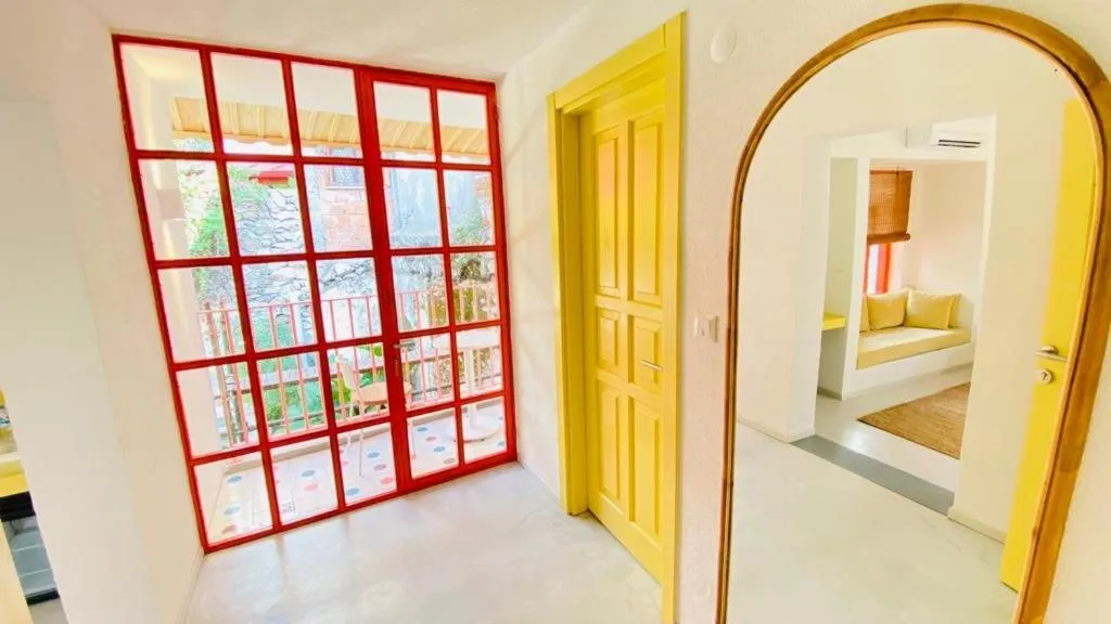 Intérieur lumineux avec une grande fenêtre rouge et une porte jaune ouverte sur un espace de détente.