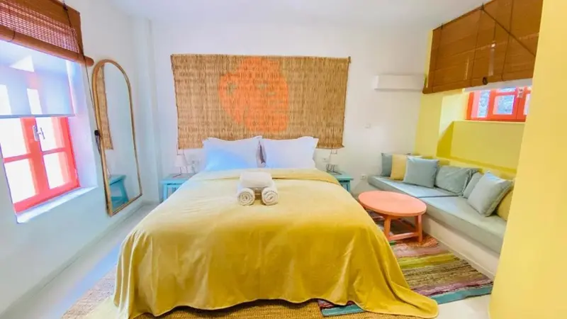 Une chambre lumineuse avec un lit recouvert d'un drapé jaune et un coin salon intégré.