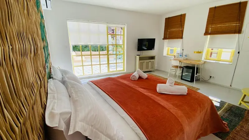 Une chambre lumineuse avec un lit recouvert d'une couverture orange et un bureau.