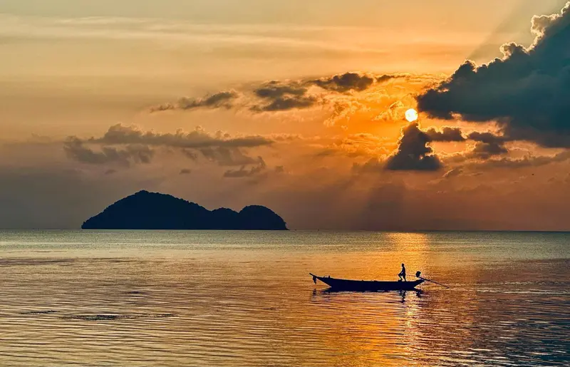 Un coucher de soleil illumine la mer et une silhouette rame sur un bateau.