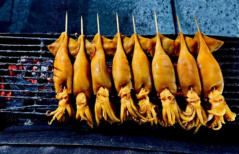 Brochettes de calamars grillés sur un barbecue.