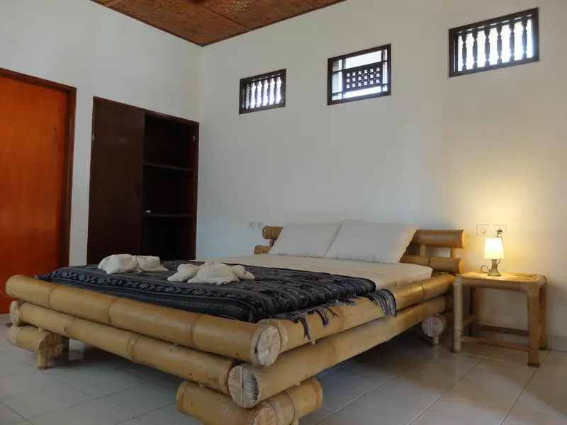 Une chambre lumineuse avec un grand lit en bambou et des serviettes décoratives.