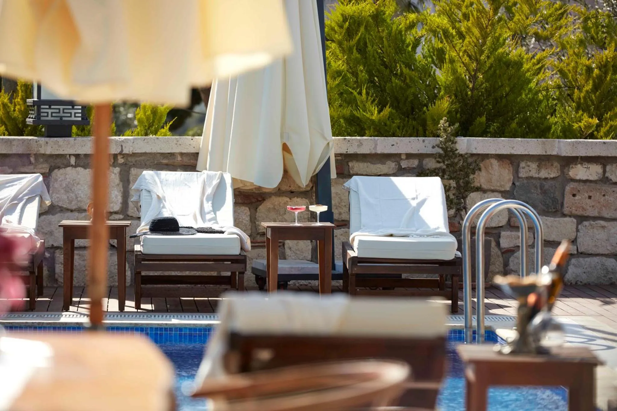 Transats et tables basses sur une terrasse ensoleillée près d'une piscine.