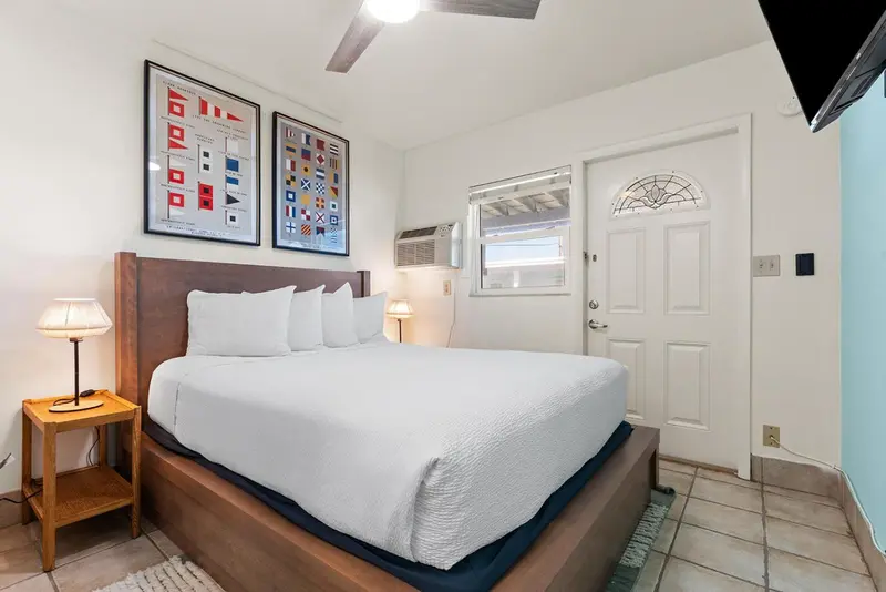 Une chambre lumineuse avec un grand lit blanc et deux tableaux décoratifs au mur.